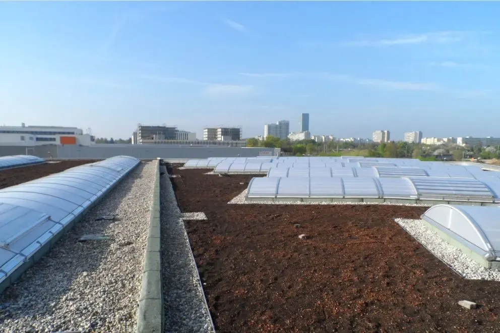 Blick über ein großes Flachdach mit Lichtkuppeln, im Hintergrund die Münchner Skyline